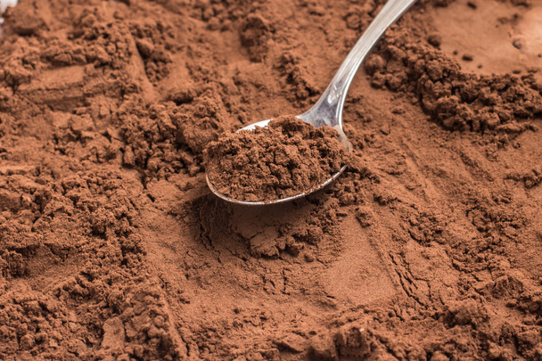 Cocoa powder into a spoon over a cocoa background. - Fotografie, Obrázek