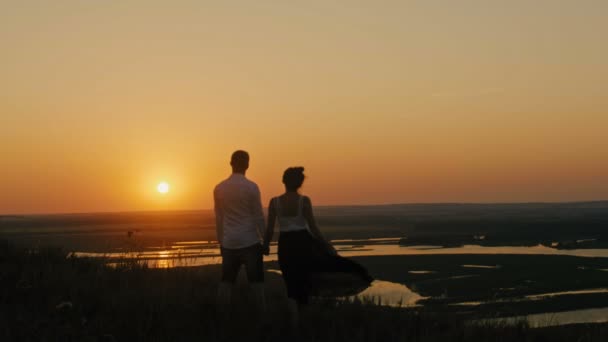 αγαπώντας ζευγάρι - παλικάρι αντρειωμένο και όμορφο κορίτσι στέκεται πάνω σε ψηλό λόφο και ψάχνει να ηλιοβασίλεμα σιλουέτα - Πλάνα, βίντεο
