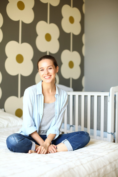 Young woman sitting on the bed near childrens cot. - Photo, Image