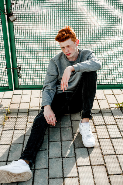 One young handsome red haired fashionable boy standing near stadium in sunny day outdoor , wearing casual clothing - Foto, immagini