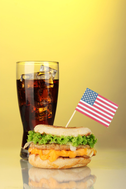 Tasty sandwich with american flag and cola, on yellow background - Фото, изображение