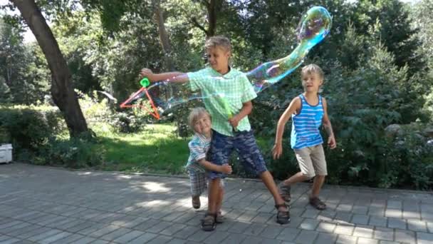 Tři kluci hrát s velké mýdlové bubliny v parku - Záběry, video