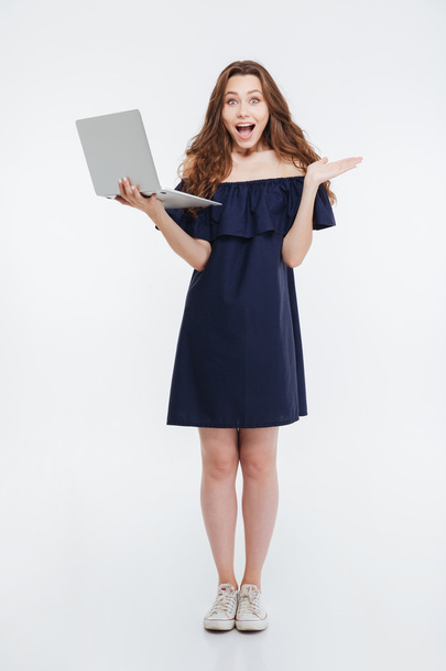 Happy excited young woman standing and holding laptop - 写真・画像