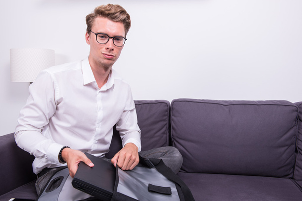 Junger Geschäftsmann packt seine Tasche auf Couch - Foto, Bild
