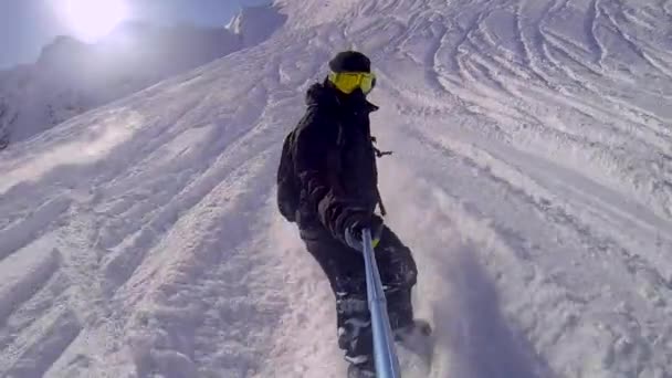Man riding on snowboard with selfie gopro stick in his hand - Footage, Video