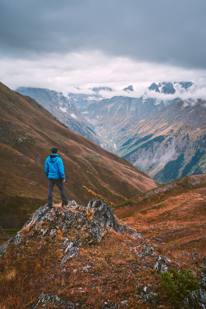 Turista de jaqueta azul em pé sobre uma rocha nas montanhas
 - Foto, Imagem
