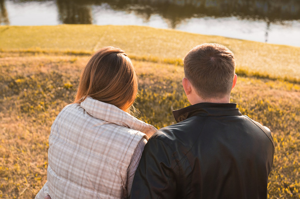 Jeune couple romantique jouissant de la nature automnale assis dans une étreinte étroite, vue de derrière
 - Photo, image
