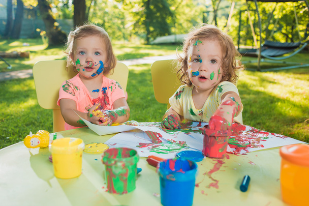 Two-year old girls painting with poster paintings together against green lawn - Zdjęcie, obraz
