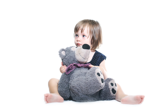 trauriges kleines Mädchen spielt mit einem Teddybär im blauen Kleid - Foto, Bild