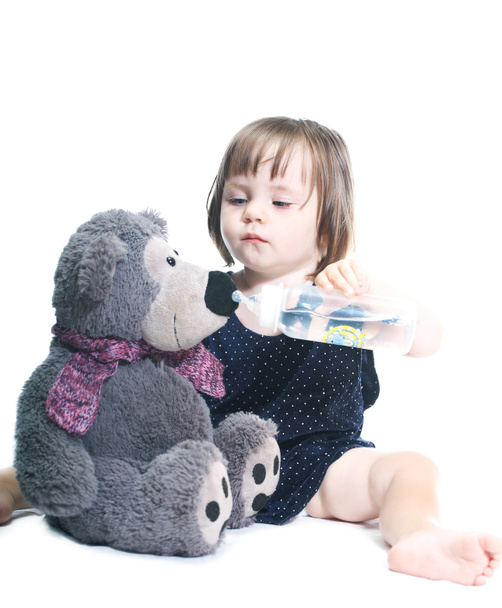 trauriges Mädchen in blauem Kleid, das mit einem Teddybär spielt, trinke es aus  - Foto, Bild