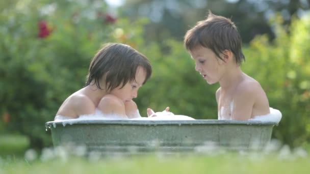 Two children, boy brothers, having a bath outdoors, making soap bubbles, summertime - Video