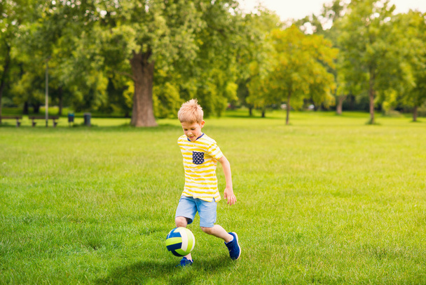 Sporting boy plays football in sunny park - Foto, afbeelding