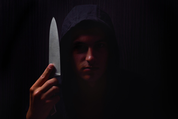Closeup portrait of a young man in a hoodie, holding a knife in  - Фото, зображення