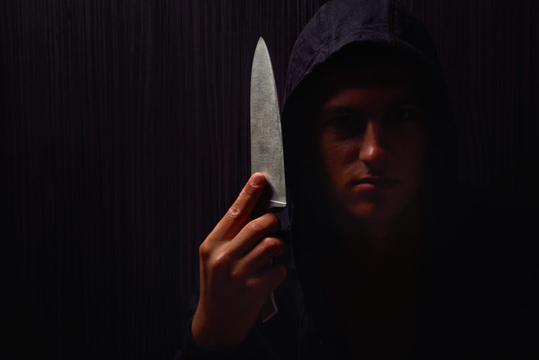Closeup portrait of a young man in a hoodie, holding a knife in  - Foto, Bild