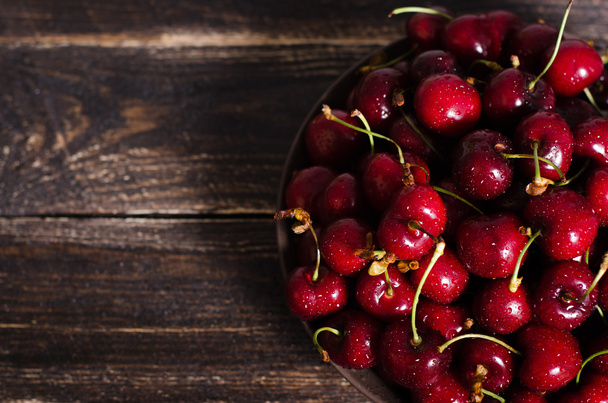 Cherries in a brown bowl on a wooden table. Free space for your text. - Photo, image