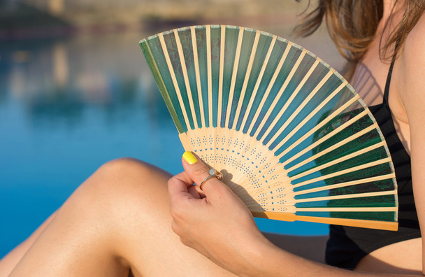 Ragazza in bikini che tiene un ventilatore a mano vicino alla piscina
 - Foto, immagini