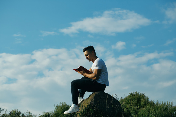 Pensive muscular man with book outdoor - Foto, Imagen