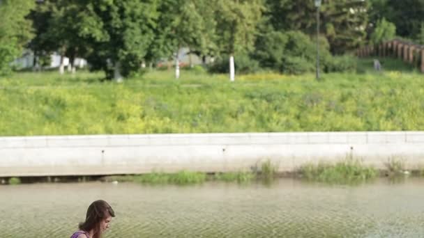 Молодая женщина что-то пишет в блокноте на берегу реки в городском парке.
 - Кадры, видео