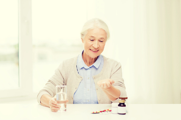 happy senior woman with water and medicine at home - Photo, Image