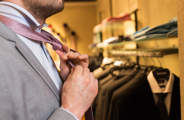 close up of man tying tie at clothing store mirror - Фото, изображение