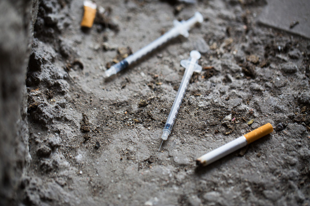 close up of syringe and smoked cigarette on ground - Foto, afbeelding