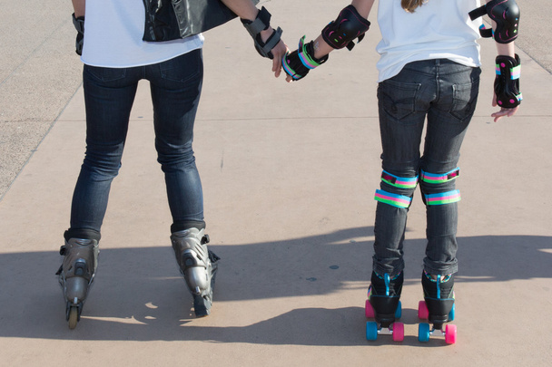 Две подружки-подростки держатся за руки катаясь на роликах
 - Фото, изображение