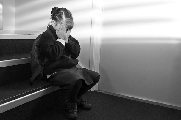 Upset young girl (age 6-7) with school uniform and backpack sitting on a staircase, crying. Children education concept. copy space - Photo, Image