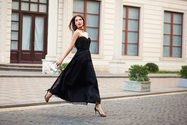 eautiful fashionable young woman in long dress running with bag. - Фото, изображение