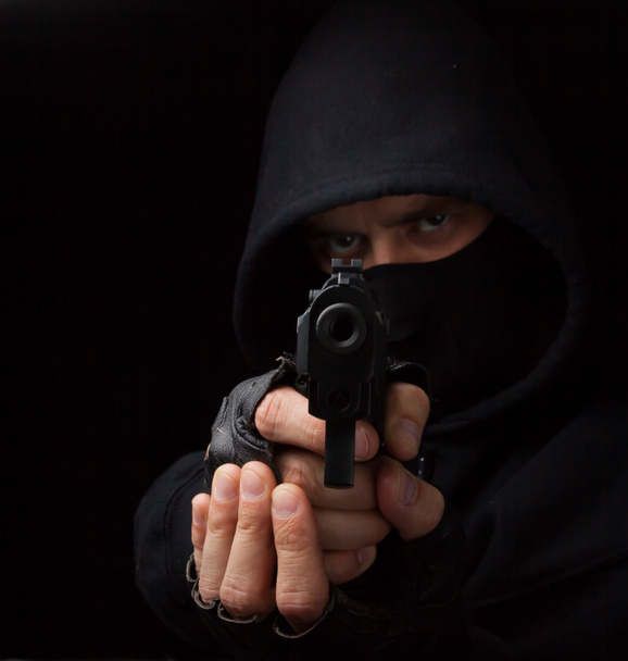 Маскований грабіжник з пістолетом прицілюється в камеру
 - Фото, зображення
