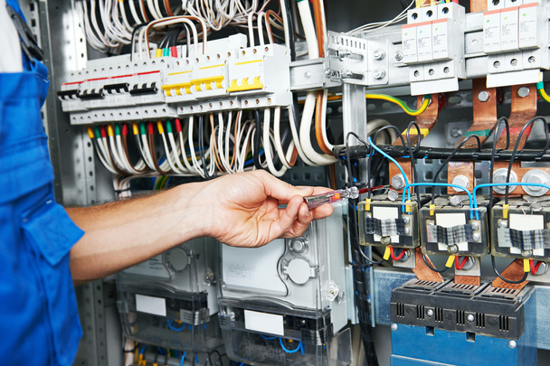 electrician works with electric meter tester in fuse box - Foto, afbeelding