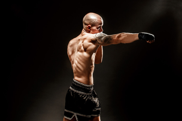 Muscular kickbox or muay thai fighter punching in darkness - Foto, Bild
