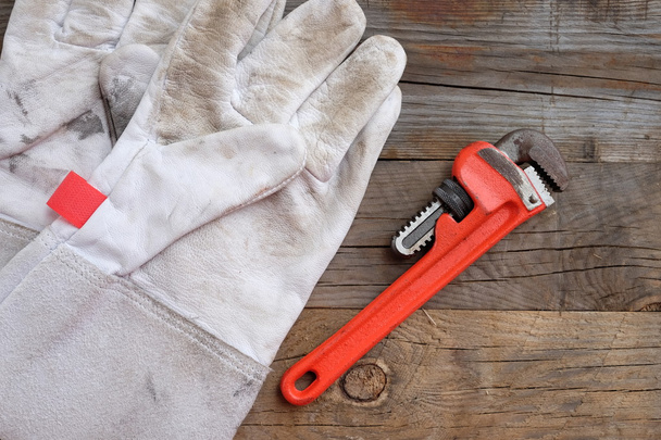 White leather gloves and pipe wrench on wooden background. - 写真・画像