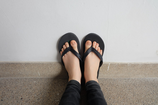 junge Mädchenbeine in schwarzen Flipflop-Sandalen auf dem Boden oder Grunge  - Foto, Bild