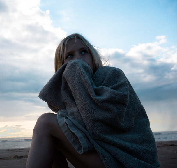 sad girl sitting on the rocks the beach wrapped in a towel - Фото, изображение