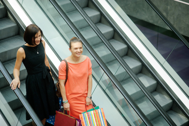 Two beautiful young girlfriends on the escalator at the Mall. - Foto, afbeelding