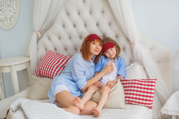 朝母と幼い娘がベッドの上に座る - 写真・画像