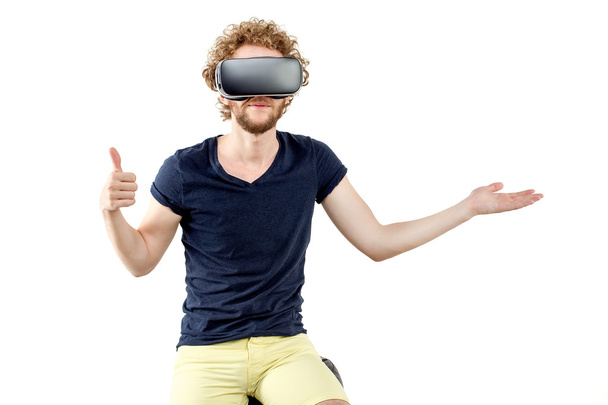 Joven hombre de pelo rizado usando un auricular VR y experimentando realidad virtual aislado sobre fondo blanco
 - Foto, Imagen