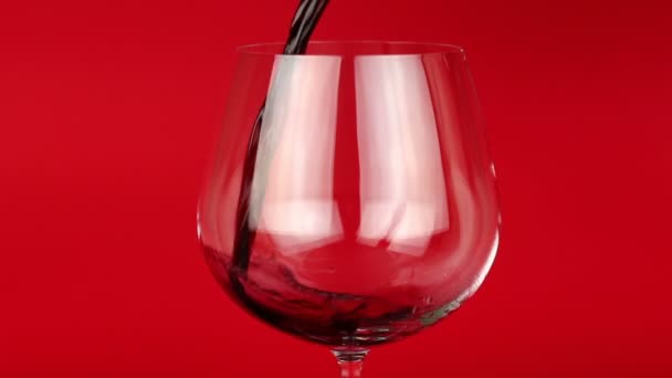 Červené víno nalil do sklenice na červeném pozadí - Záběry, video