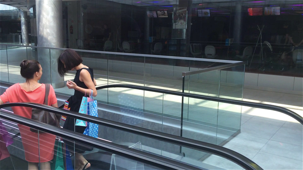 zwei Mädchen, die die Treppe auf der Rolltreppe in einem Einkaufszentrum hinuntergehen, Freundinnen, die in einem Geschäft einkaufen, Frauen, die im Geschäft einkaufen - Filmmaterial, Video