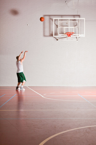 Tough healthy young man playing basketball in gym indoor. Wearing white shirt and green shorts. - Foto, imagen
