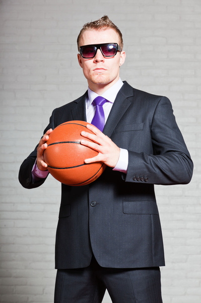 Hombre de negocios con baloncesto. Llevando gafas de sol oscuras. Joven guapo con el pelo corto y rubio. pared de ladrillo blanco
. - Foto, Imagen