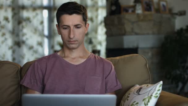 Vakava hyvännäköinen mies työskentelee hänen laptop istuessaan sohvalla olohuoneessa
 - Materiaali, video
