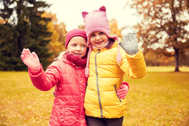 two happy little girls waving hand in autumn park - Fotoğraf, Görsel