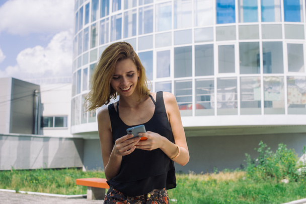 Young slim girl in a black T-shirt using smartphone sitting in the yard - Fotografie, Obrázek