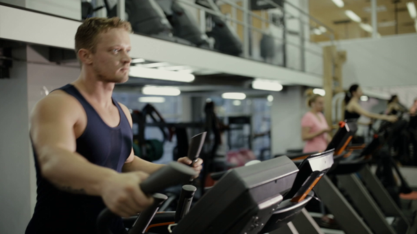 Atleta do sexo masculino fazendo exercício cardio no aparelho de treinamento no ginásio
 - Filmagem, Vídeo