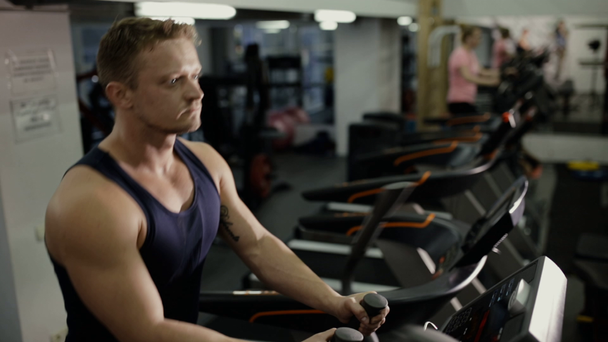 Erkek atlet spor salonunda eğitim cihazları üzerinde kardiyo egzersiz yaparak - Video, Çekim