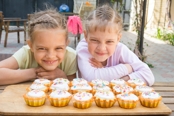Two girls pretending funny faces, sitting in front of easter cupcakes - Photo, Image