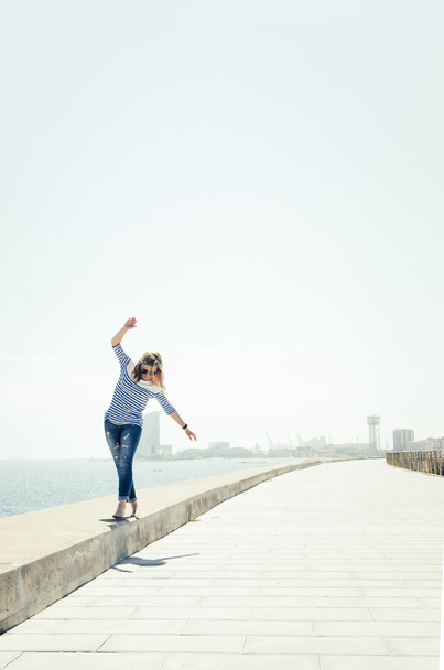 νέοι hipster γυναίκα το περπάτημα κοντά στη θάλασσα δρόμο δρόμο σύνορα με υψωμένα τα χέρια. - Φωτογραφία, εικόνα