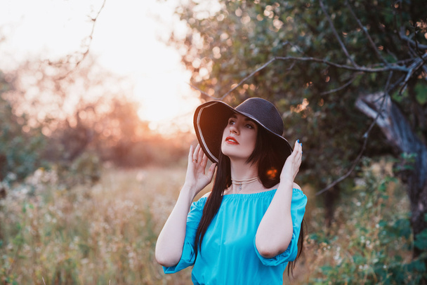 Portrait of a beautiful girl in a hat in a field in sunset light - 写真・画像