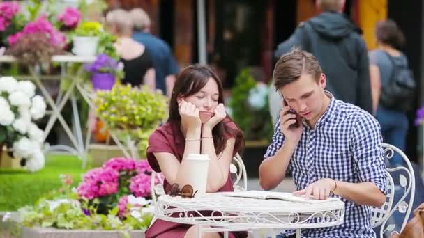 Restaurante turistas pareja en la cafetería al aire libre. Chica joven triste con su novio porque él está ocupado con las tareas
 - Imágenes, Vídeo